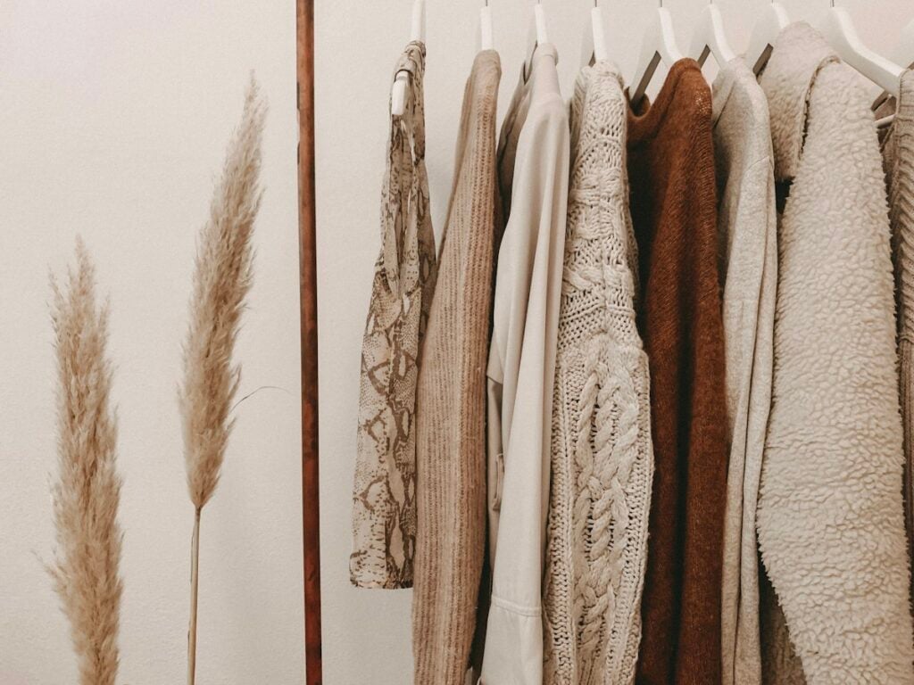 Curated brass garment rack with cozy sweaters, coats, and dried pampas grass in ceramic vase