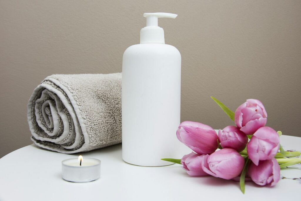 Large amber glass vessel filled with sweet almond and neroli body oil beside rolled towels